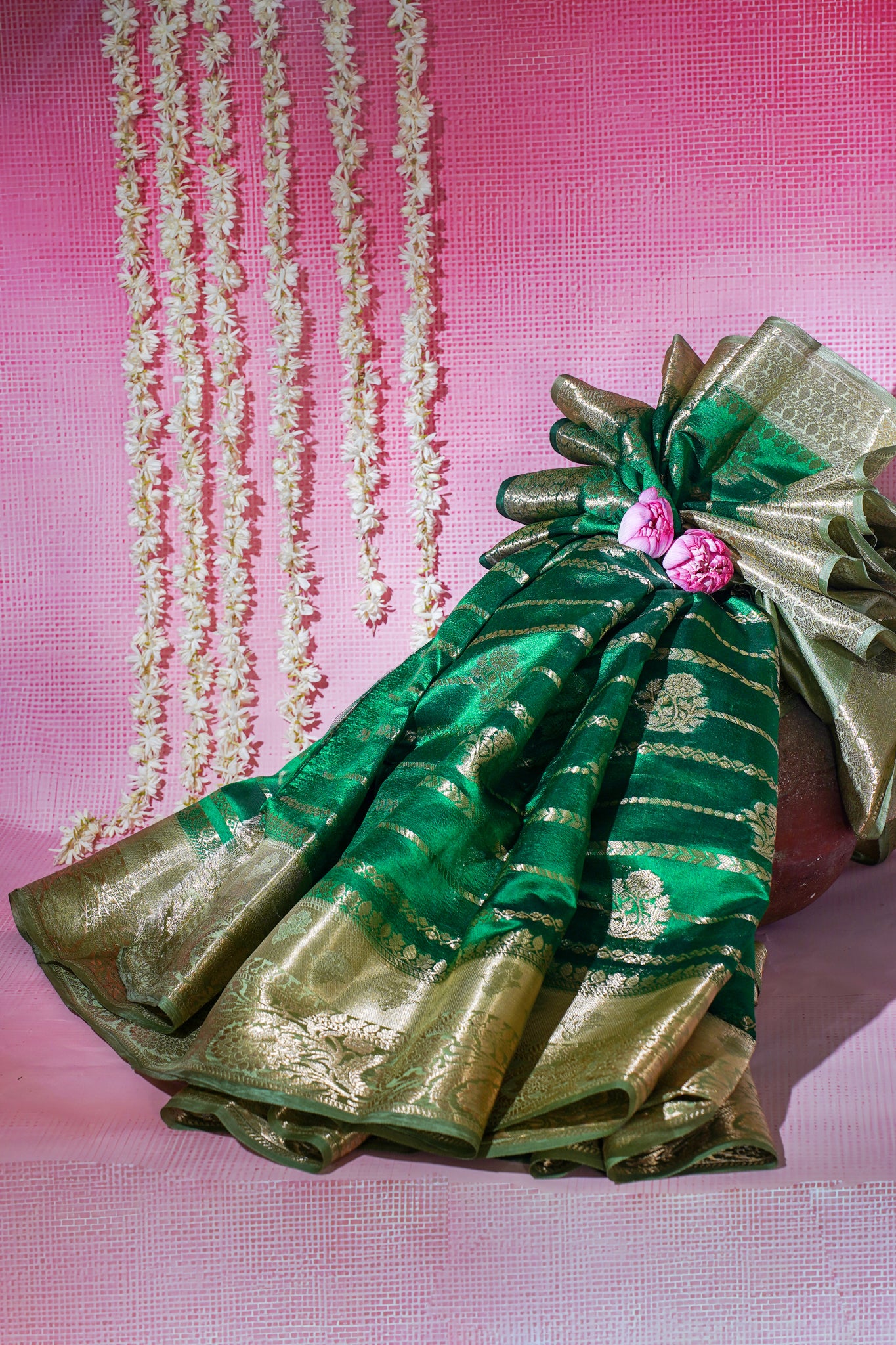 Green and gold saree with decorative elements on a pink background