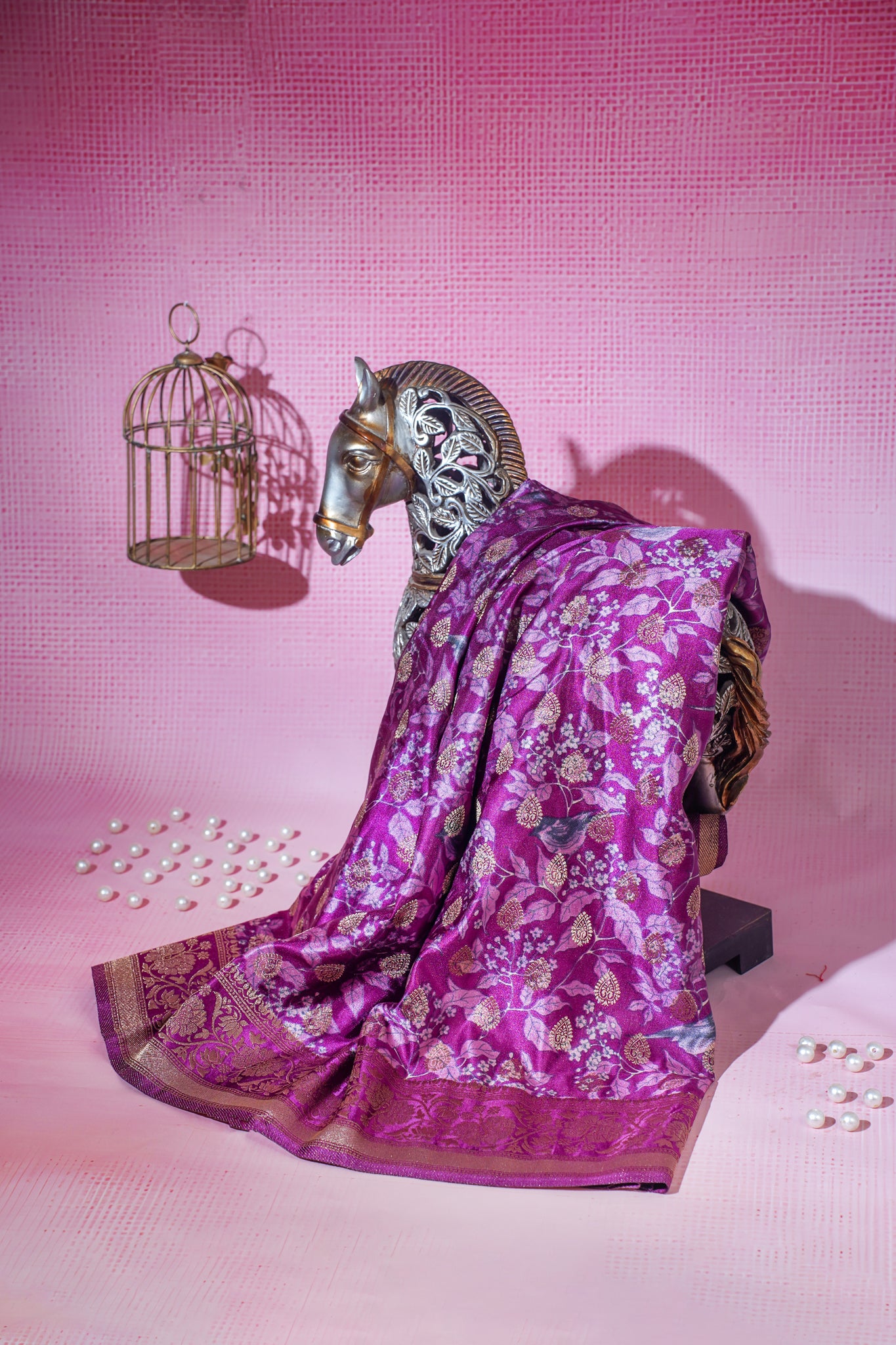 Purple saree with gold patterns draped over a horse statue on a pink background