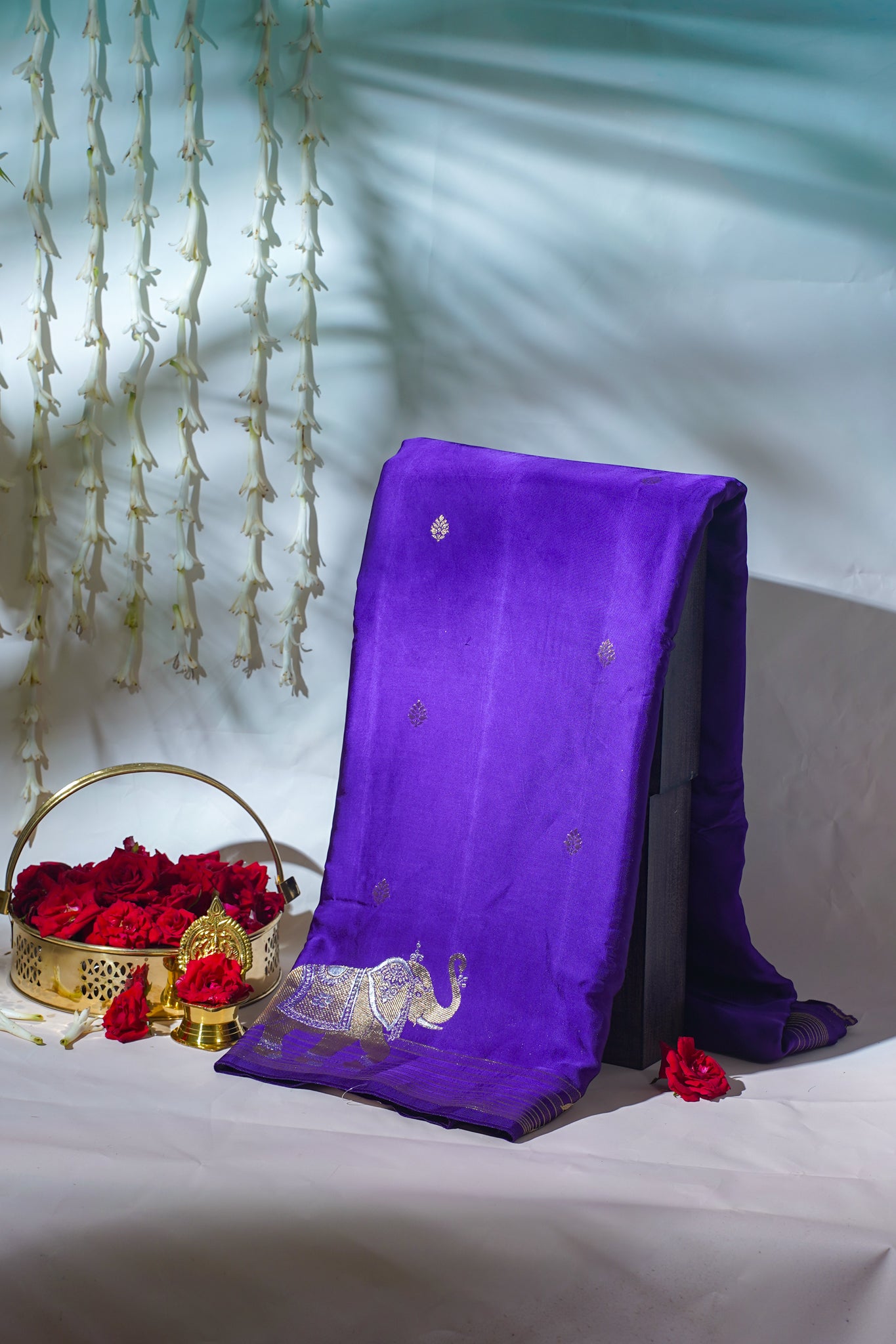 Purple fabric with gold embroidery on a white surface with red flowers and a decorative basket.