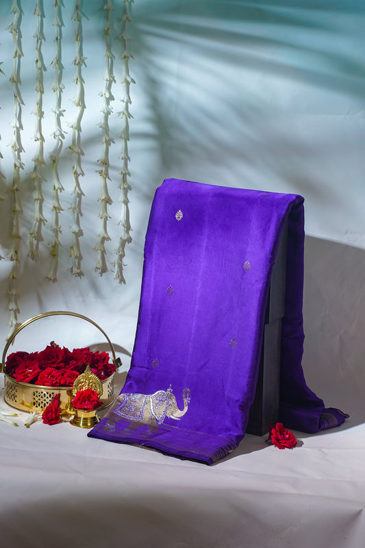 Purple fabric with gold embroidery on a white surface with red flowers and a decorative basket.