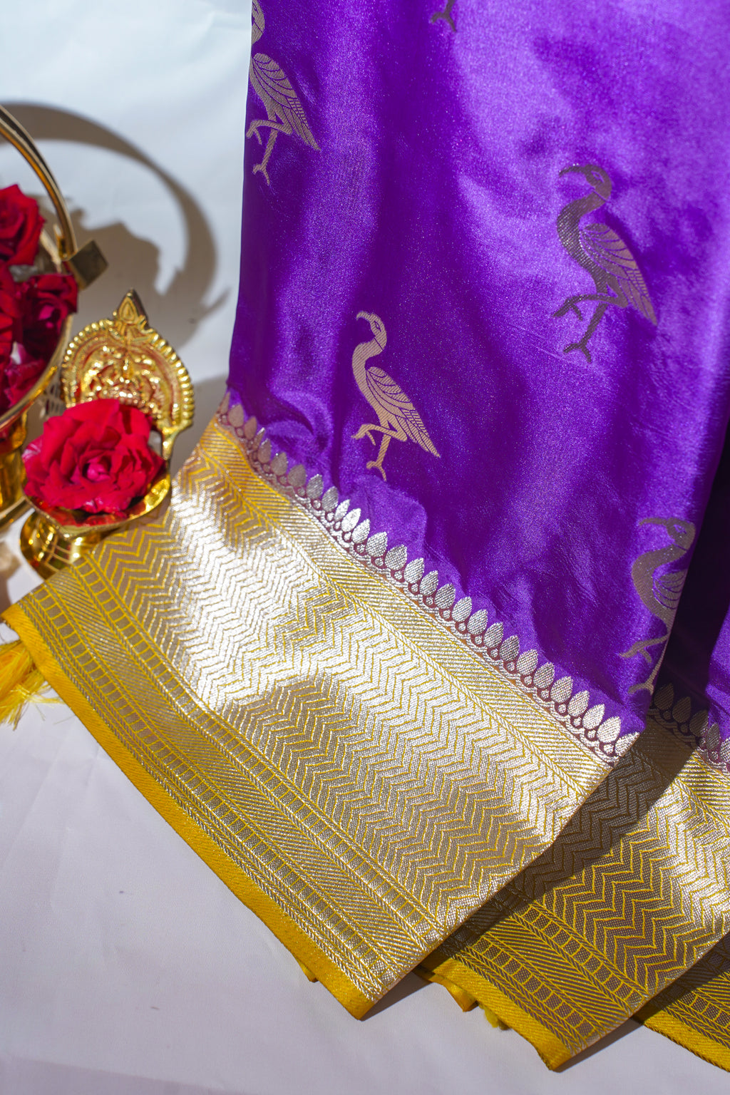 Purple saree with gold border and bird design, accompanied by red flowers and a decorative item.