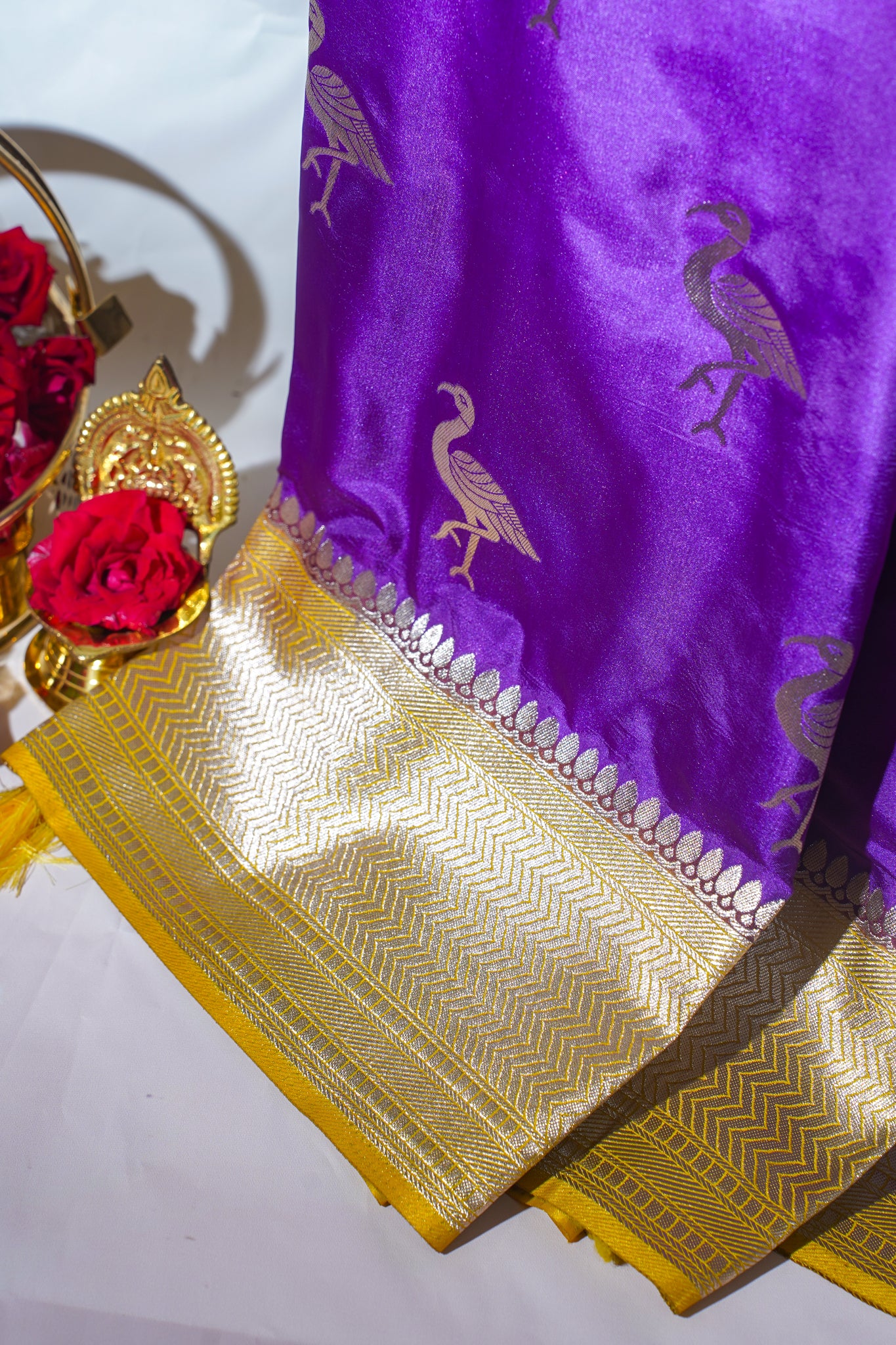 Purple saree with gold border and bird design, accompanied by red flowers and a decorative item.