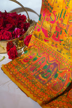 Decorative fabric with intricate patterns and colors, placed on a white surface with red flowers in the background.