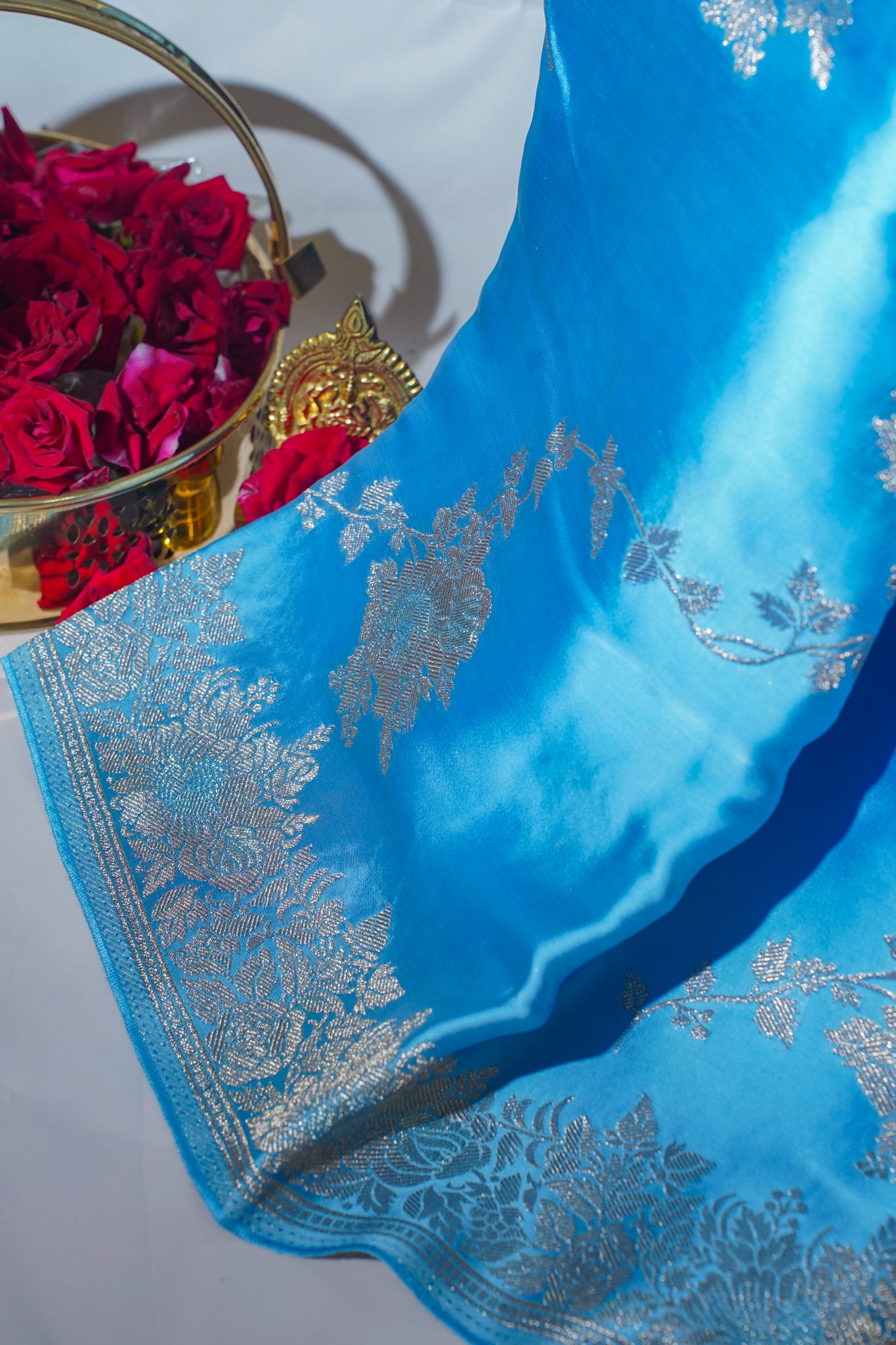 Blue saree with silver embroidery next to a basket of red flowers on a light gray background