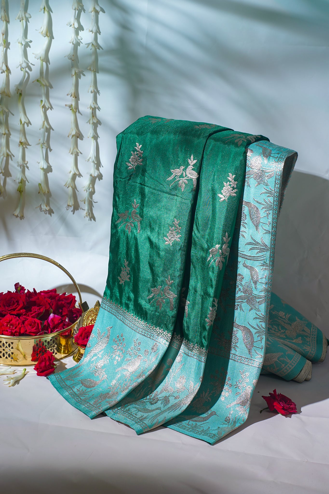 Green embroidered fabric with floral patterns on a white surface with red flowers.