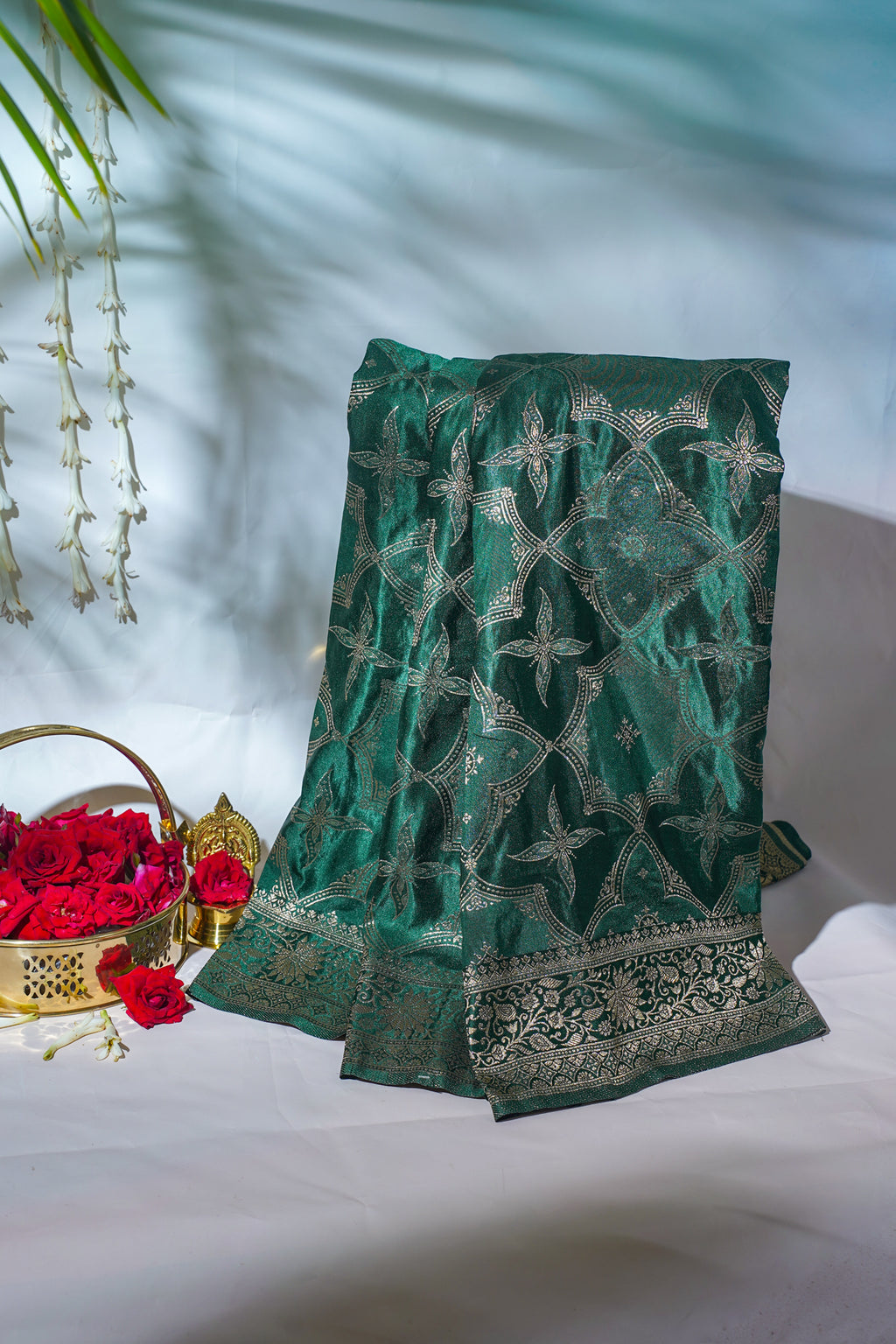 Green embroidered fabric with floral patterns on a white surface.