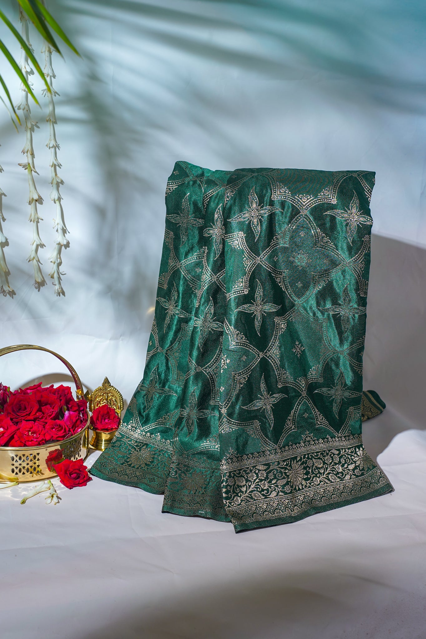 Green embroidered fabric with floral patterns on a white surface.