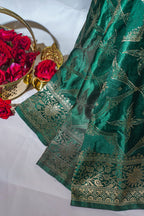 Green saree with gold patterns next to a basket of red roses on a white background