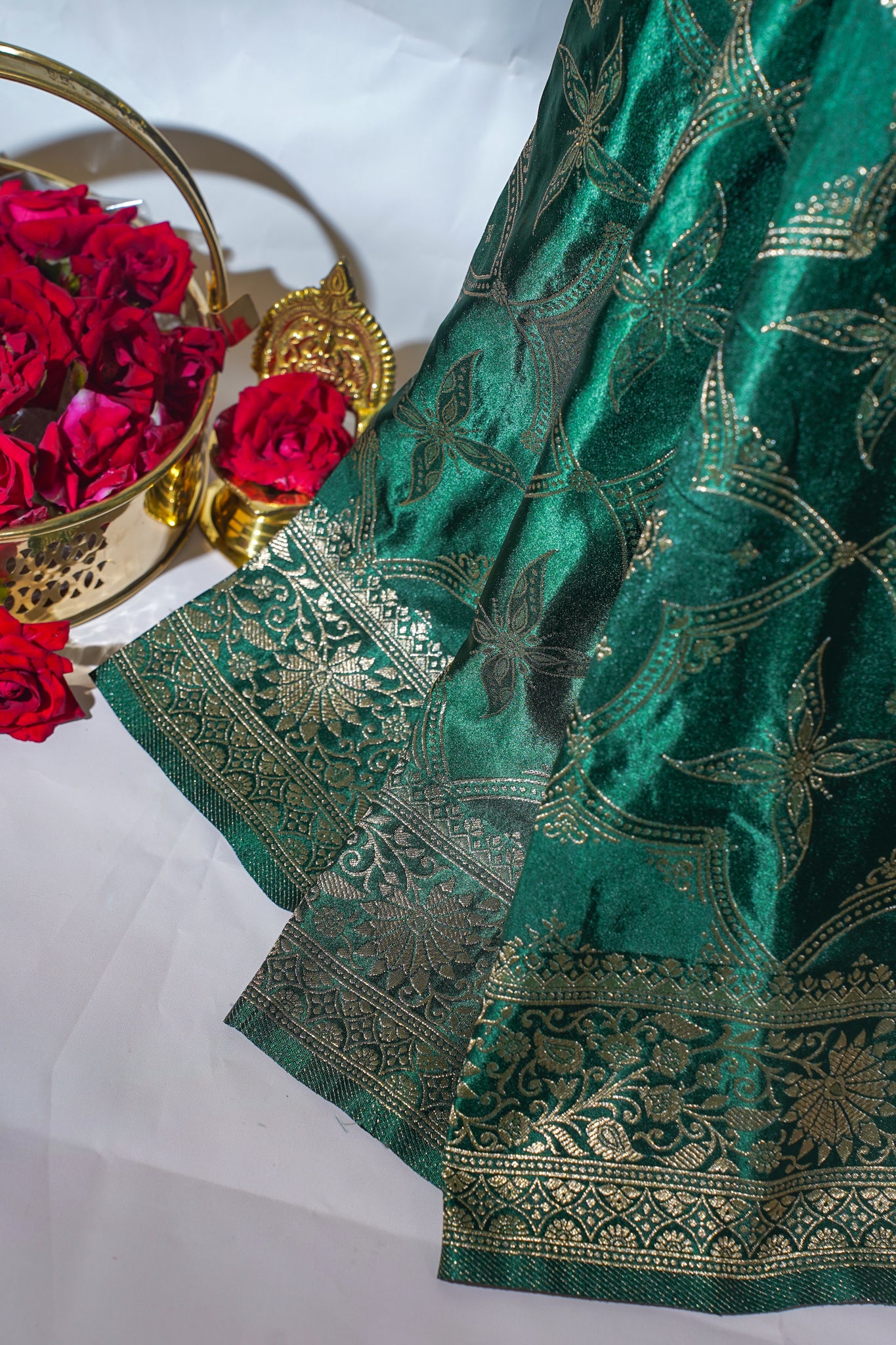 Green saree with gold patterns next to a basket of red roses on a white background