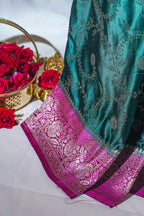 Teal saree with pink border and red roses in a gold basket on a white background