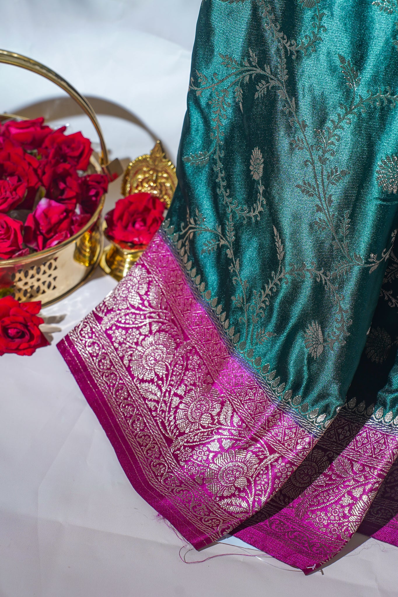 Teal saree with pink border and red roses in a gold basket on a white background