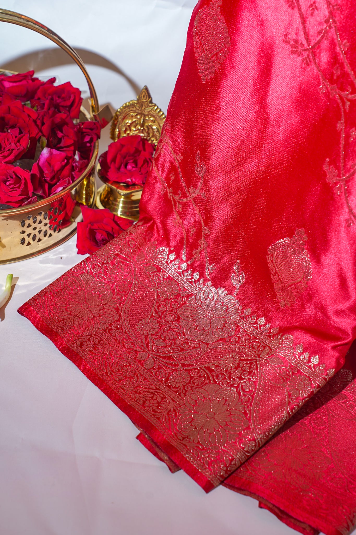 Red saree with gold embroidery next to a basket of red roses on a white background