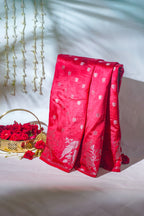Red Saree with white patterns draped over a surface, with a basket of red roses and decorative elements in the background.