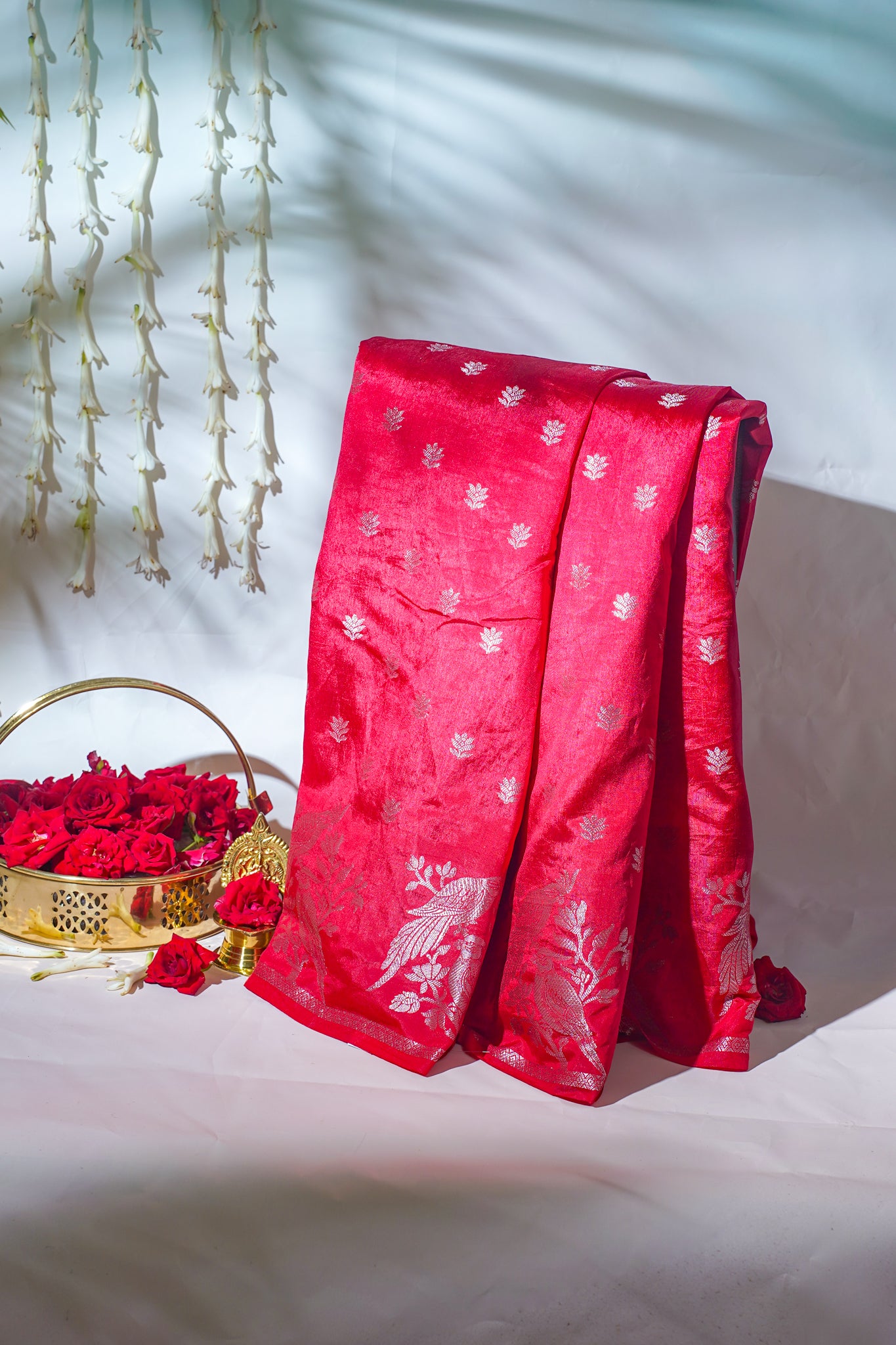 Red Saree with white patterns draped over a surface, with a basket of red roses and decorative elements in the background.