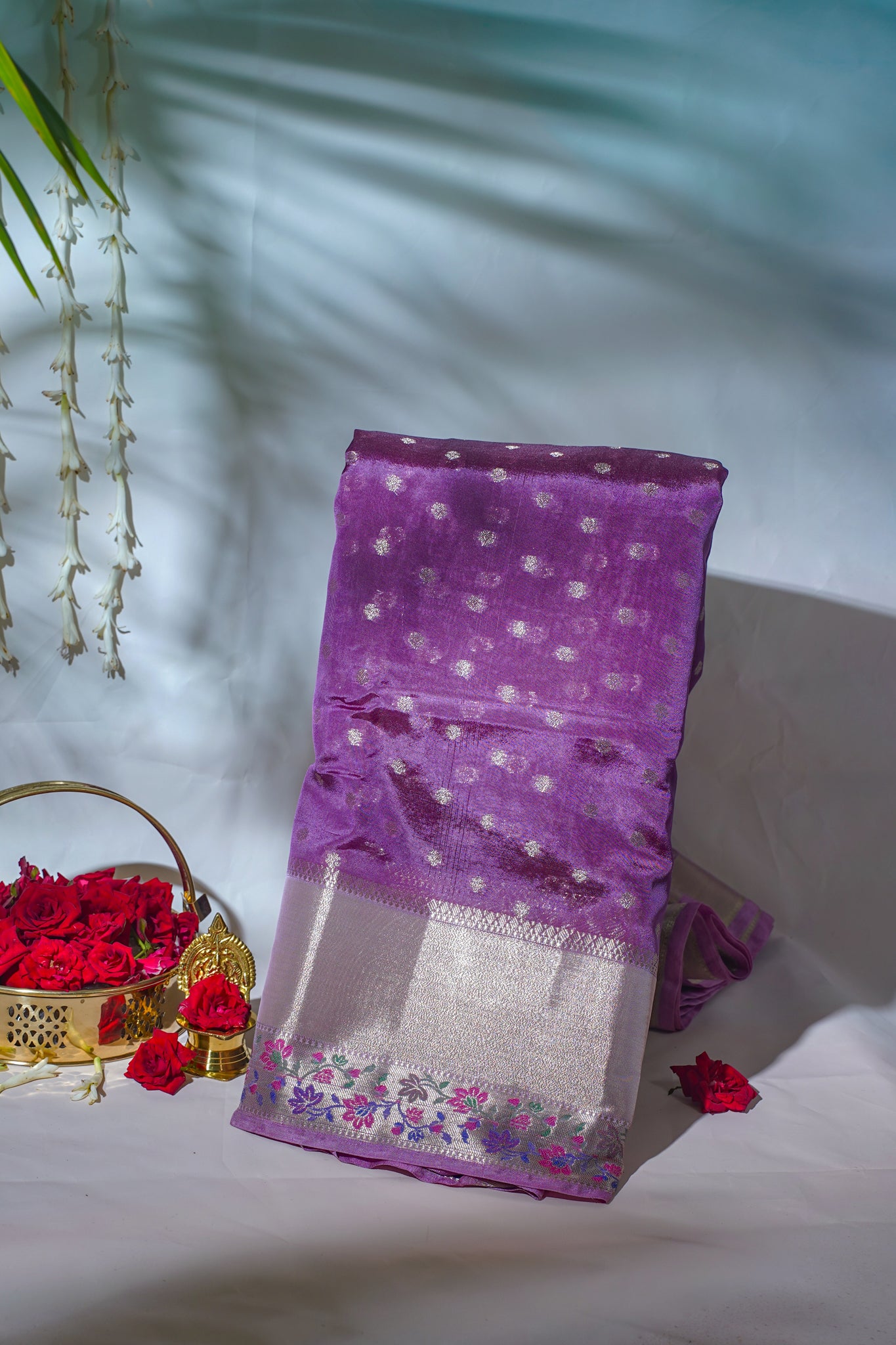 Purple saree with floral patterns on a white surface with red flowers and a gold basket.