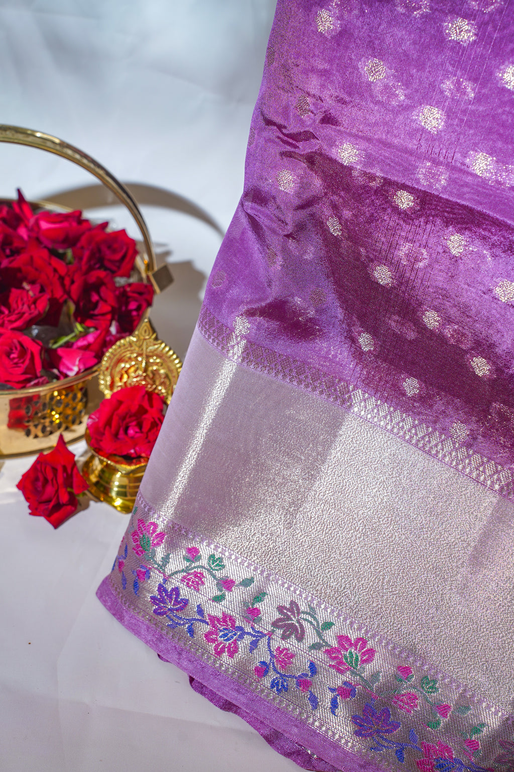 Purple fabric with floral embroidery and red roses in the background