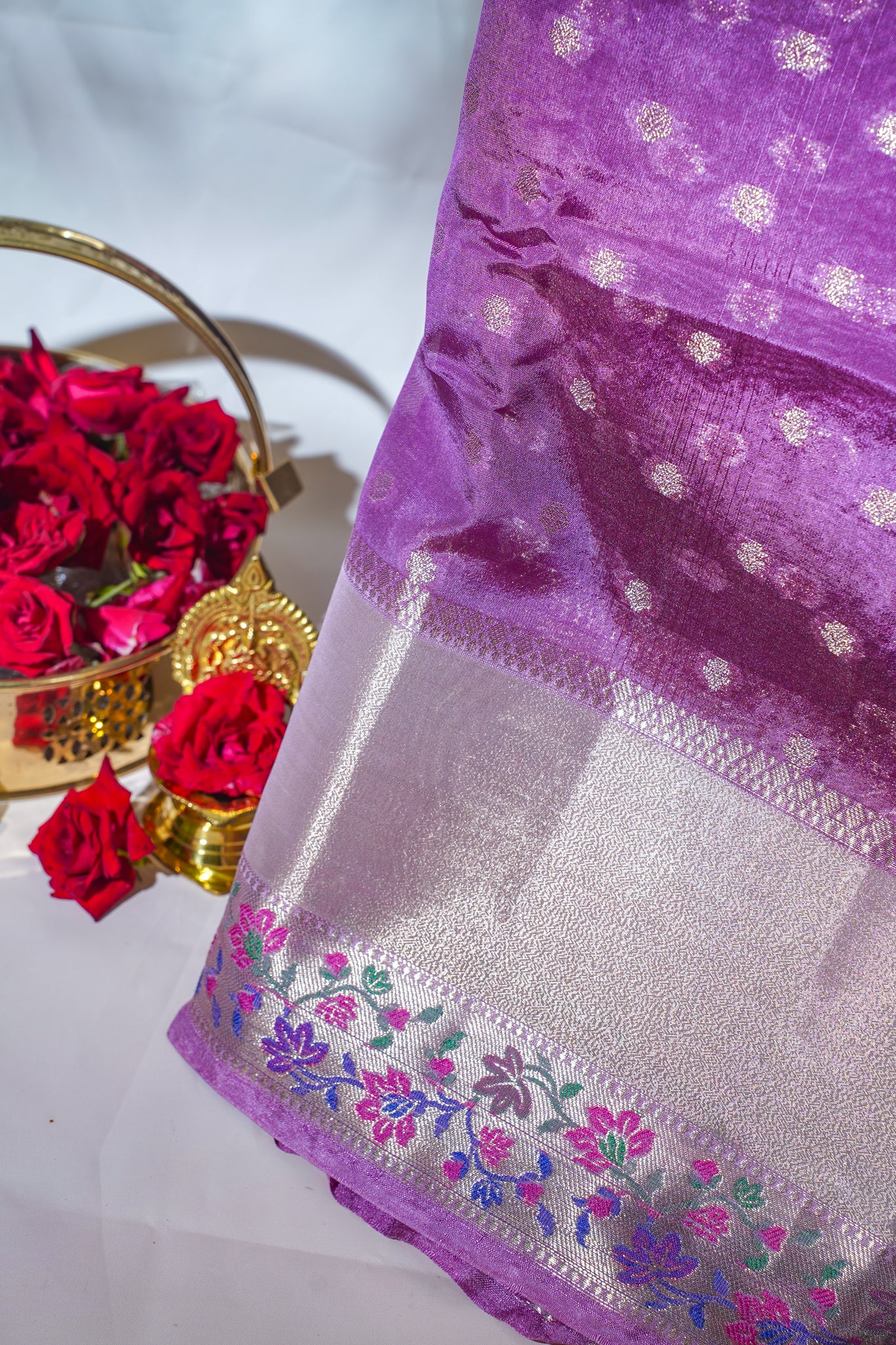 Purple fabric with floral embroidery and red roses in the background