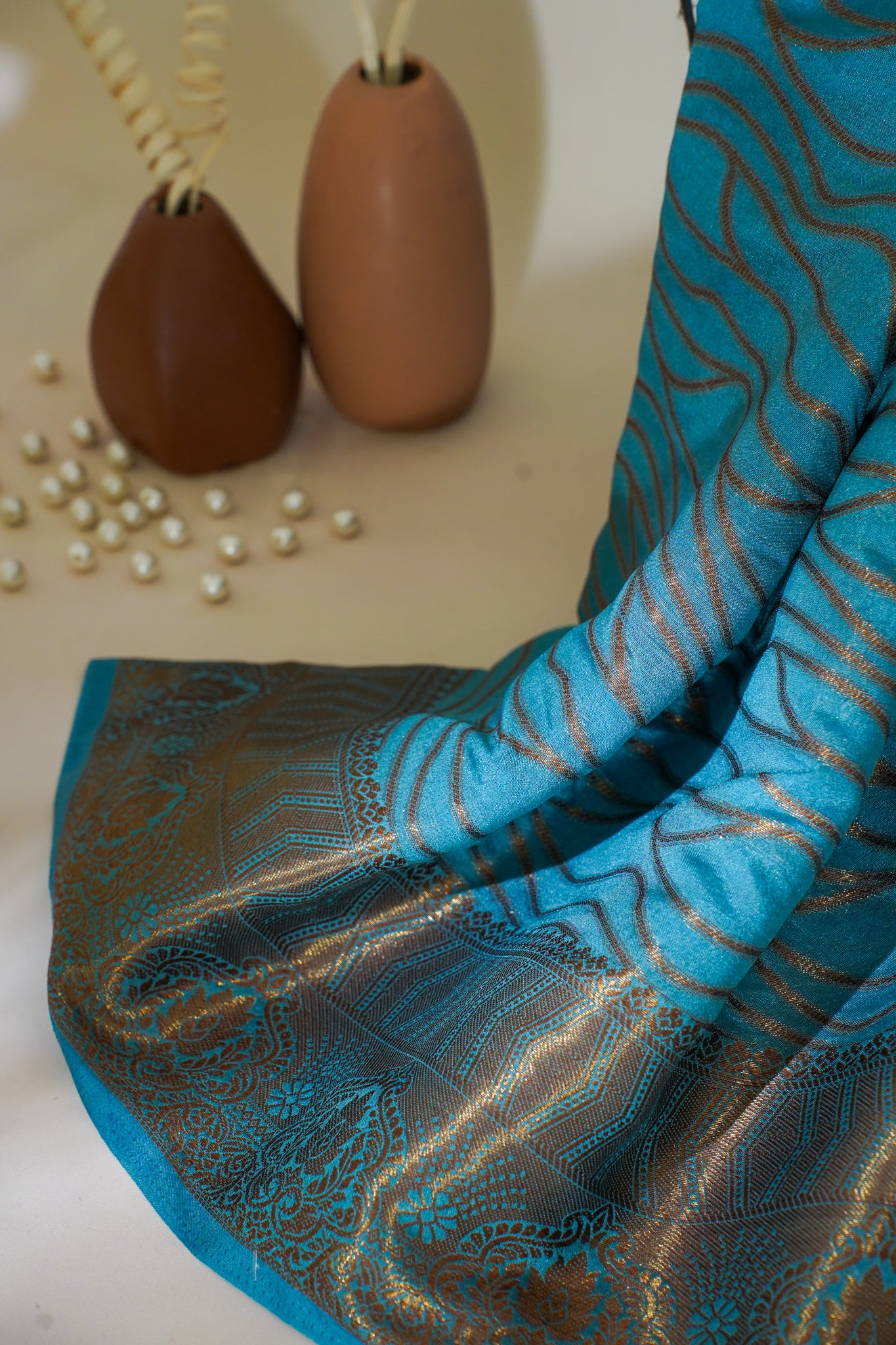 Blue and brown patterned fabric with decorative vases and pearls in the background