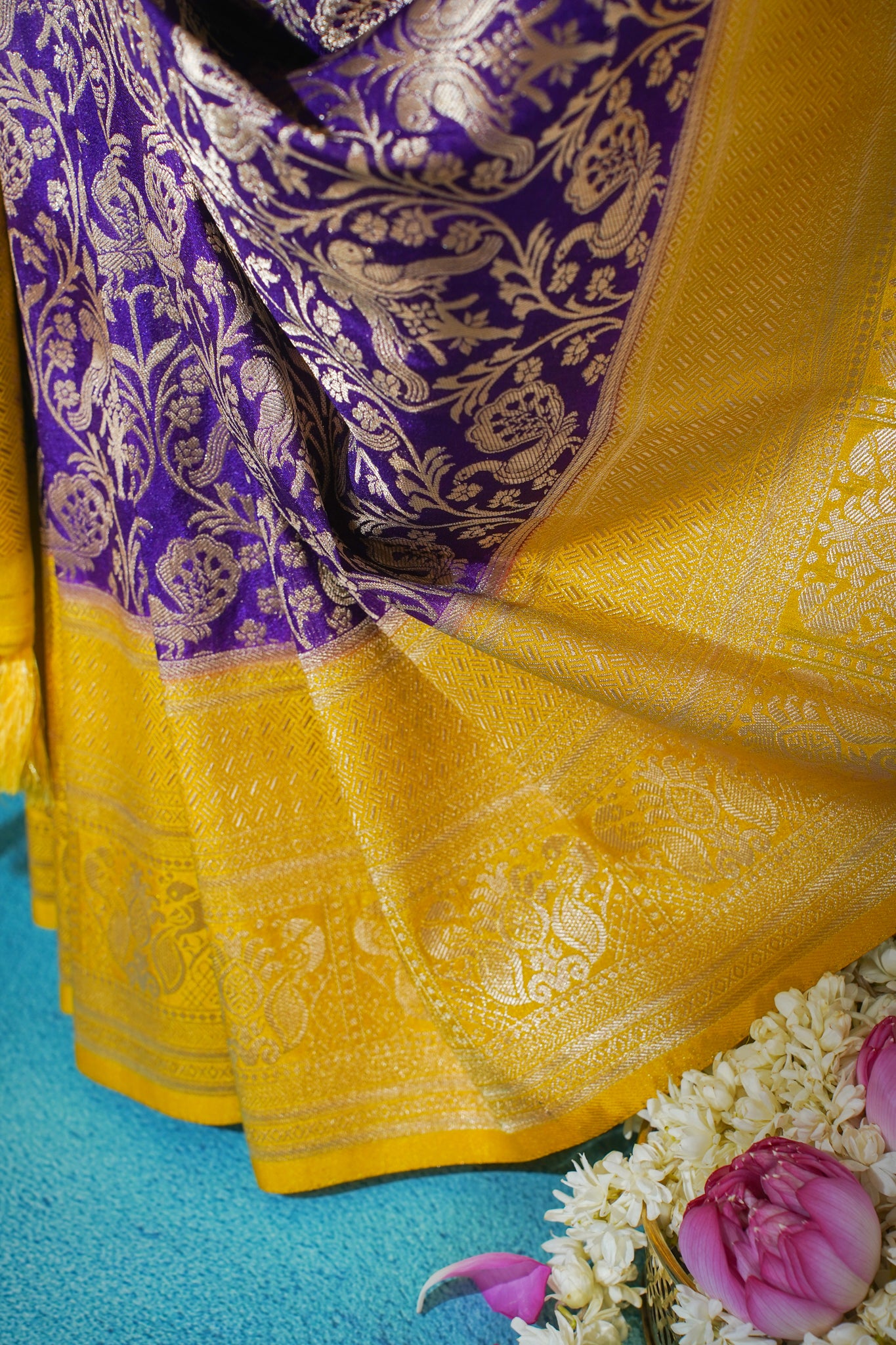 Close-up of a yellow and purple saree with floral decorations on a blue background