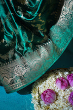 Teal saree with gold embroidery on a blue background with flowers.