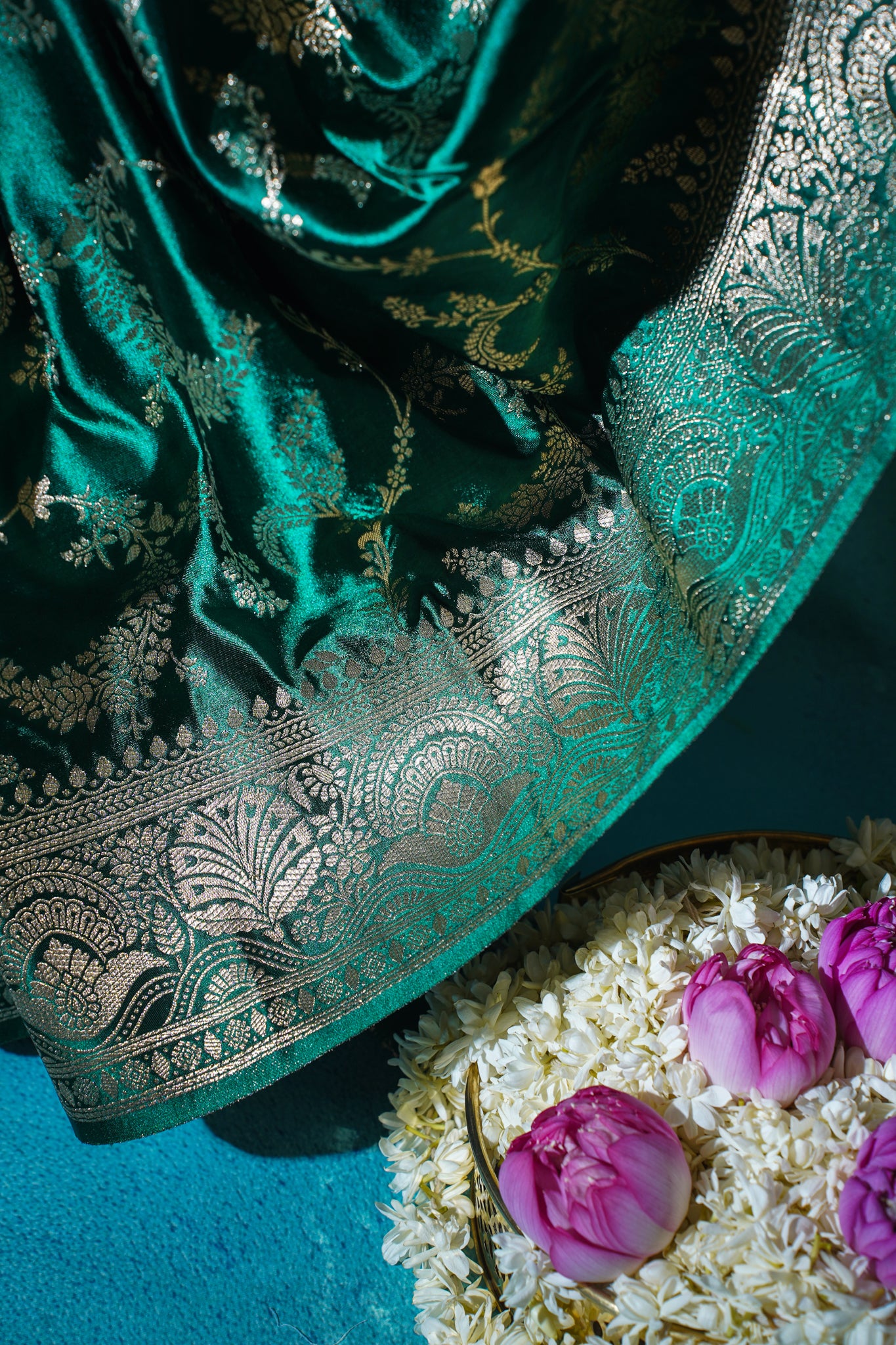 Teal saree with gold embroidery on a blue background with flowers.