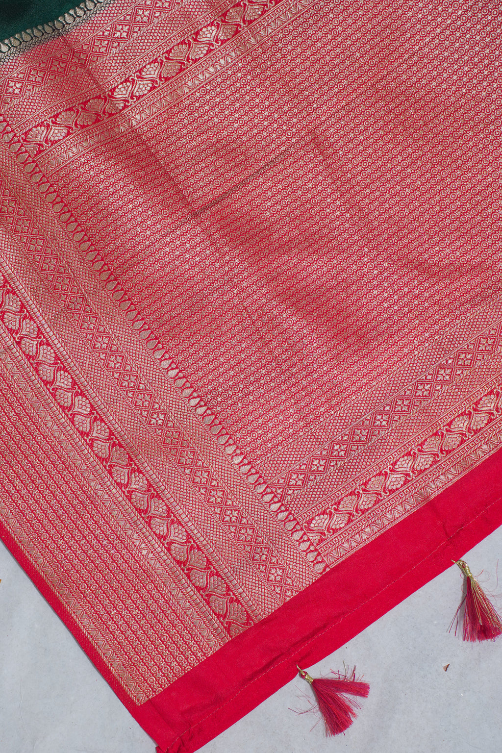 Red fabric with intricate patterns and tassels on a light gray background