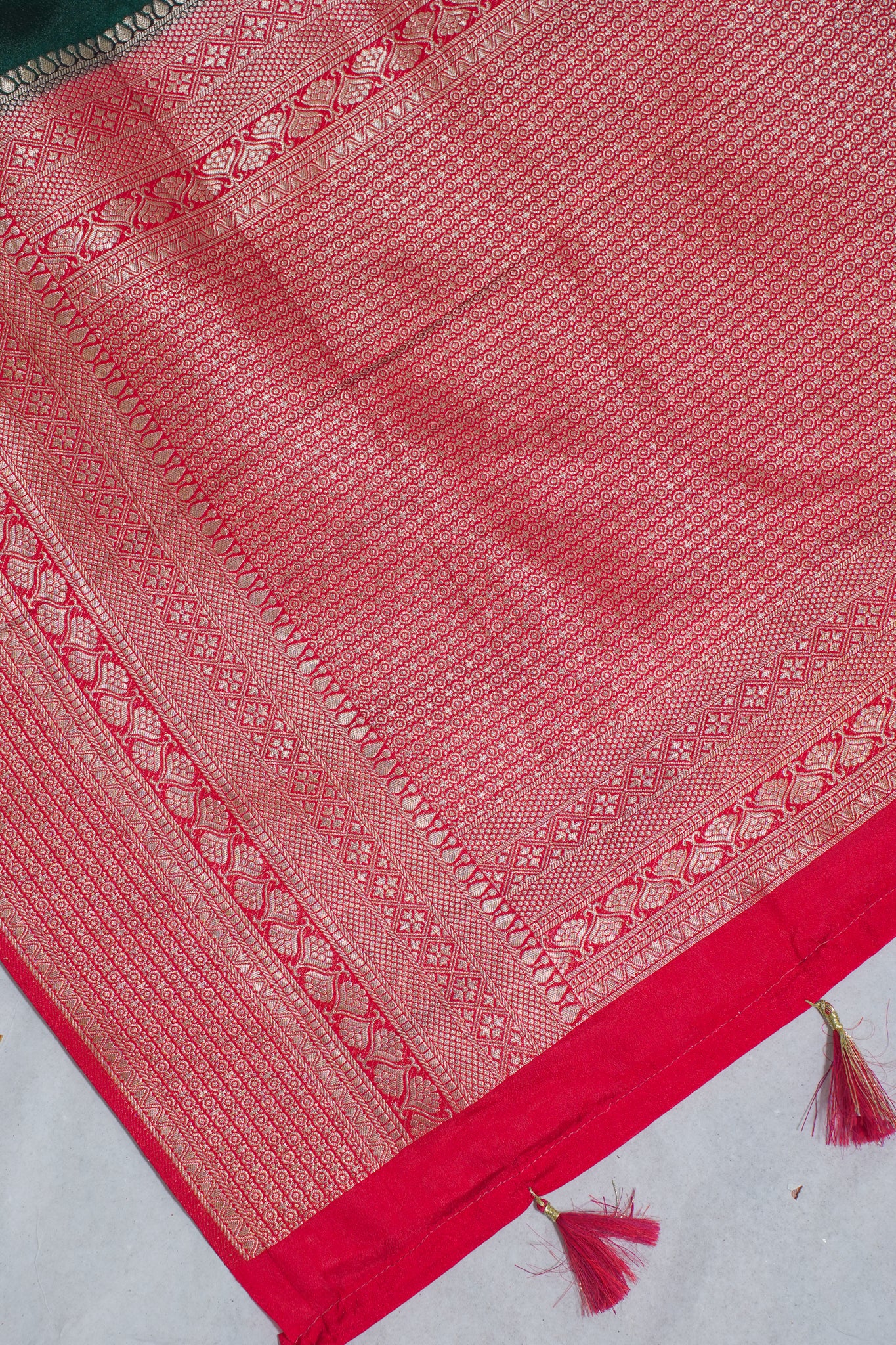 Red fabric with intricate patterns and tassels on a light gray background