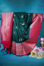 Green saree with red border draped over a blue background with flowers and a pot.