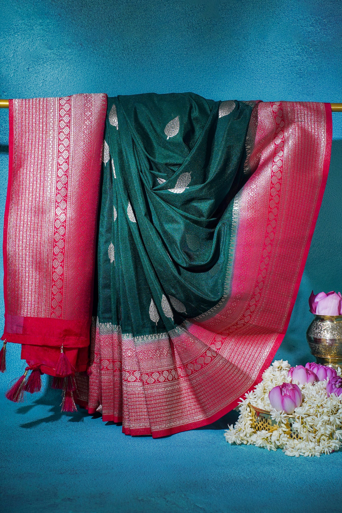 Green saree with red border draped over a blue background with flowers and a pot.