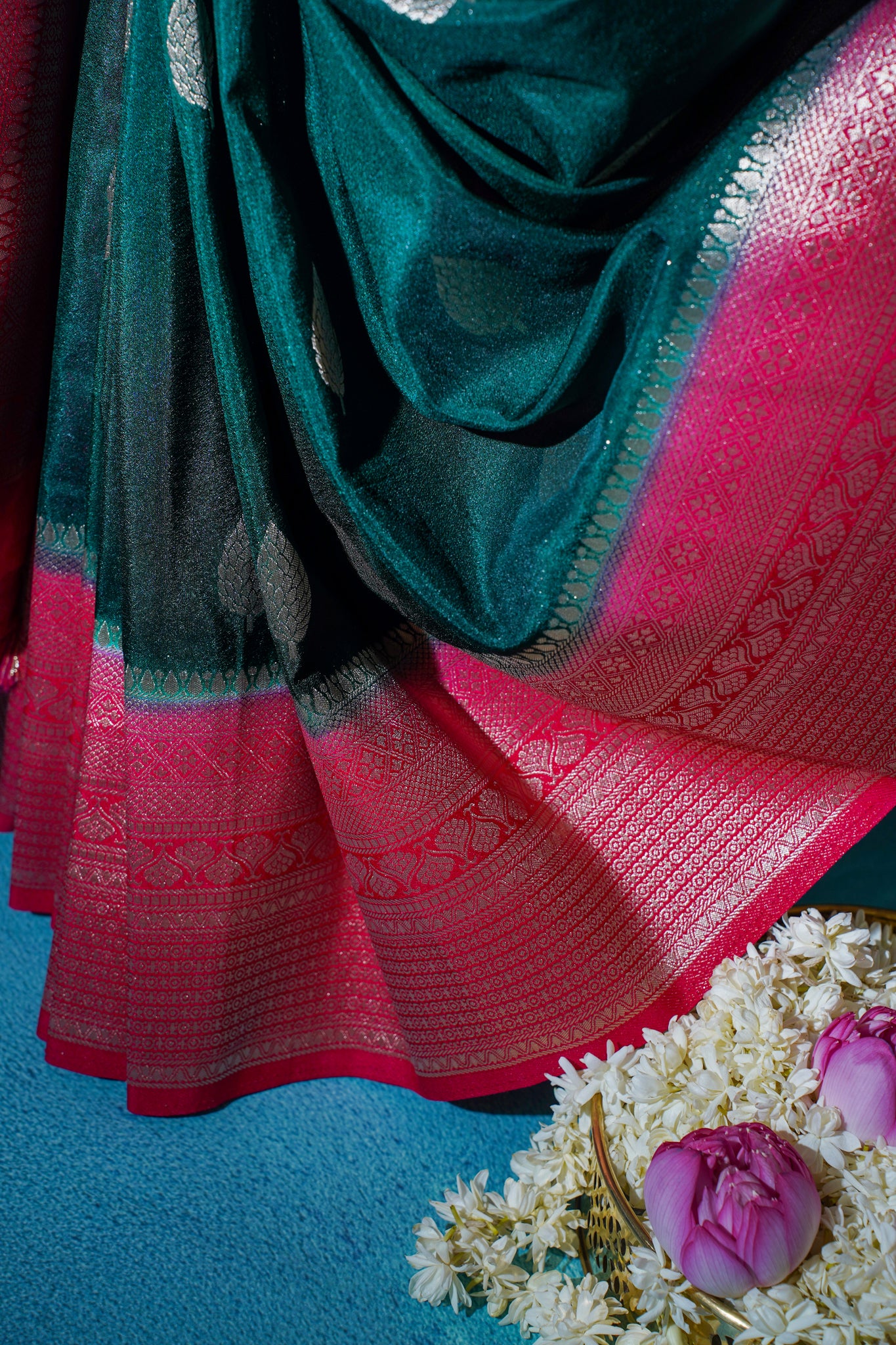 Close-up of a red and green saree with floral decorations on a blue background