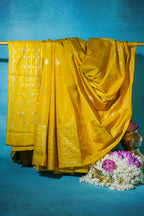 Yellow saree draped over a rod with flowers and a pot on a blue background