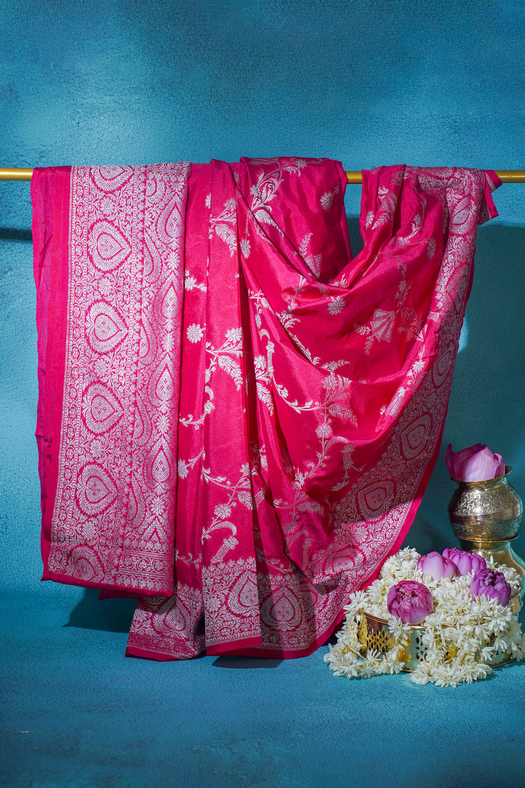 Pink saree with white patterns draped over a rod against a blue background
