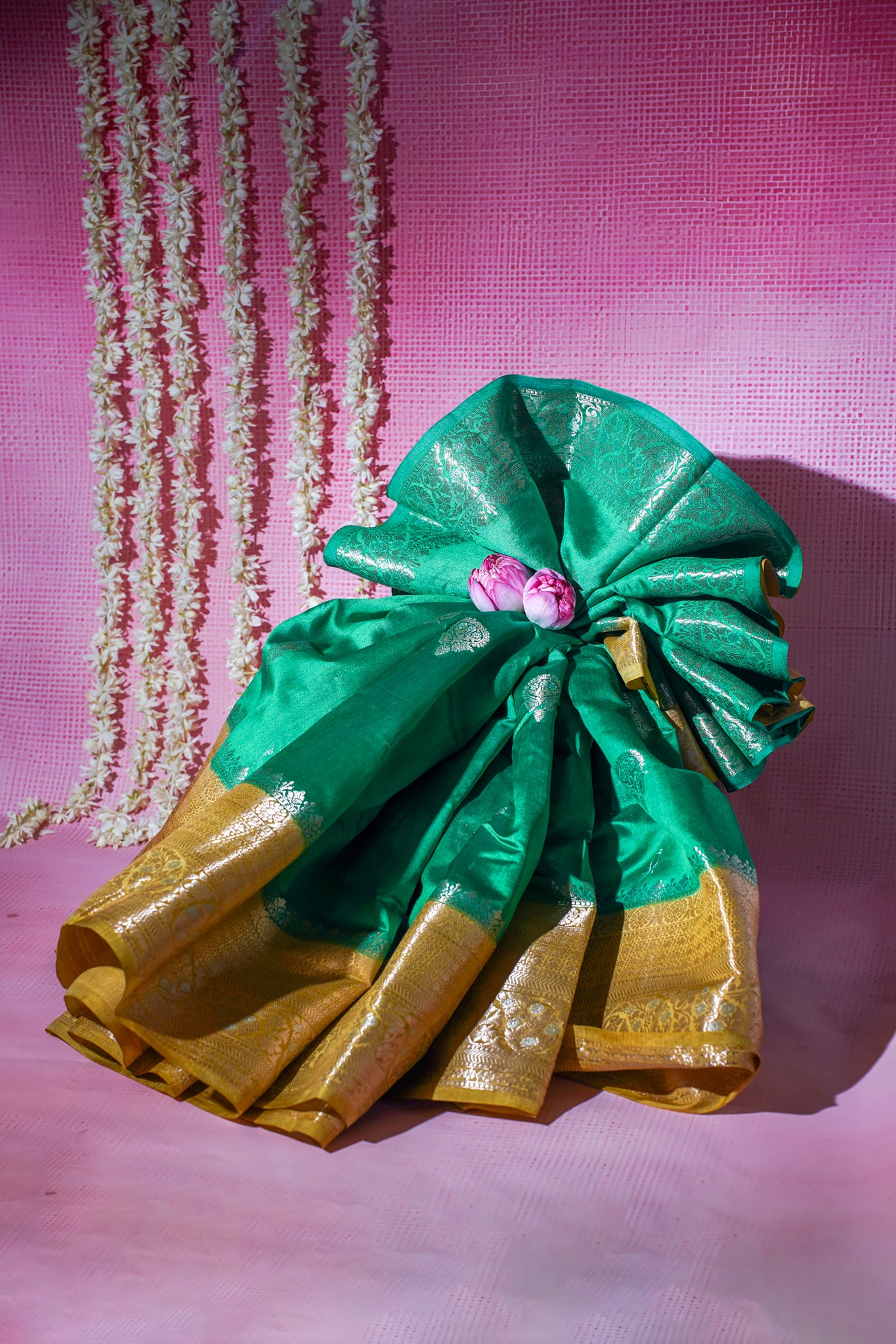 Green and gold saree with a pink flower on a pink background