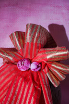 Red and gold striped bow with purple flowers on a pink textured background