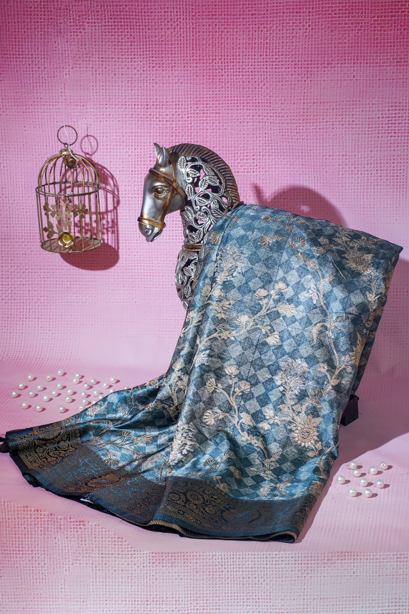 Blue saree with gold patterns draped over a horse statue on a pink background