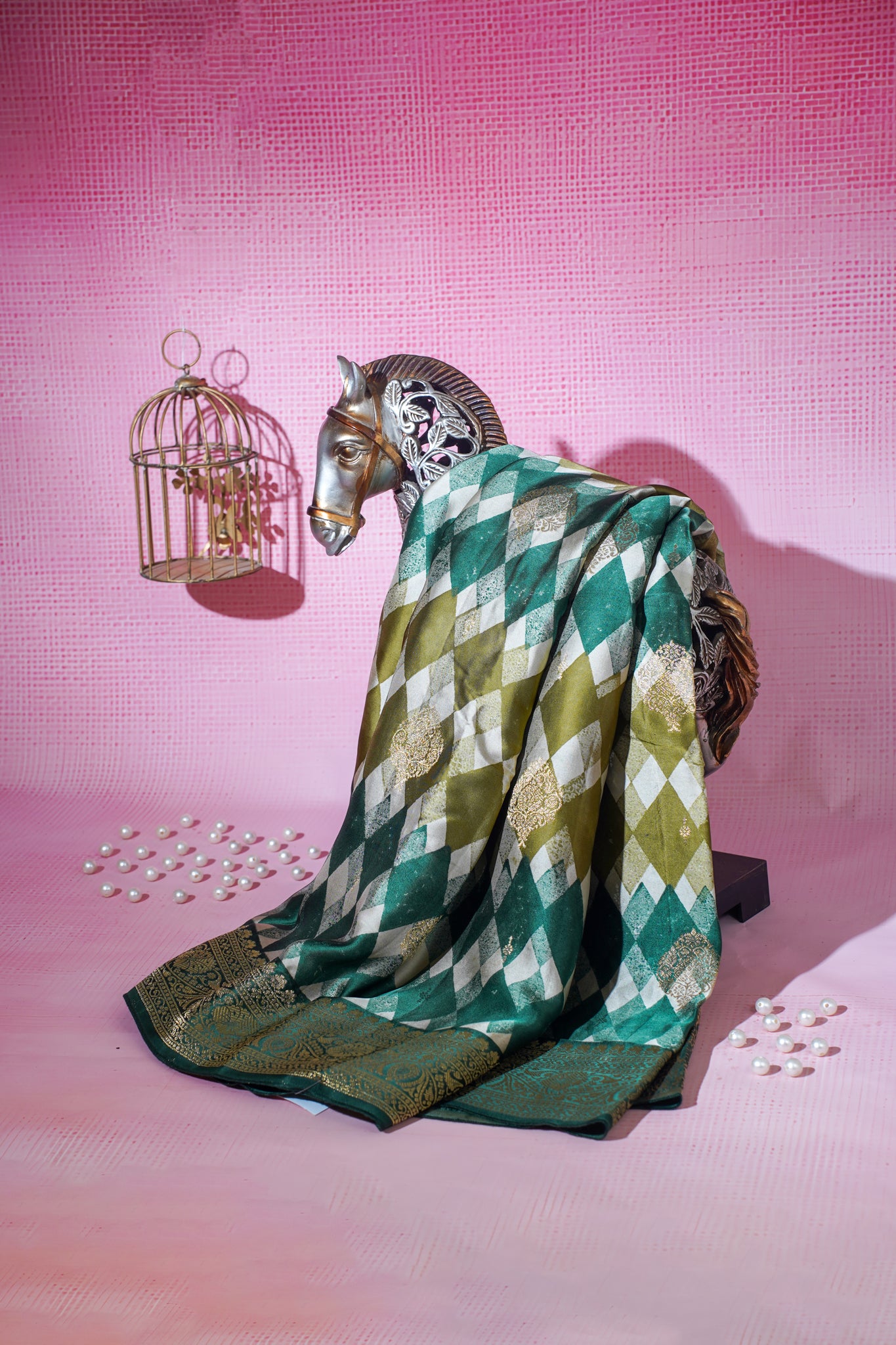 Decorative horse figurine draped with a green and white checkered Saree on a pink textured background.
