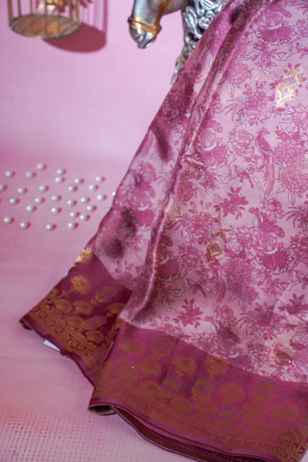 Pink saree with floral patterns and gold accents on a pink background
