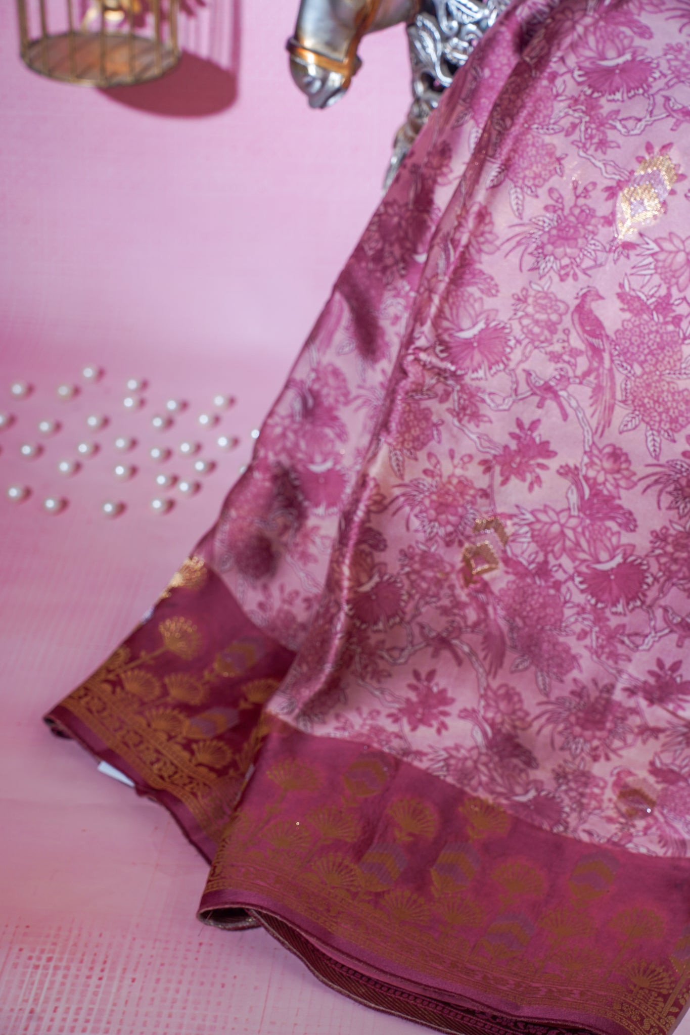 Pink saree with floral patterns and gold accents on a pink background