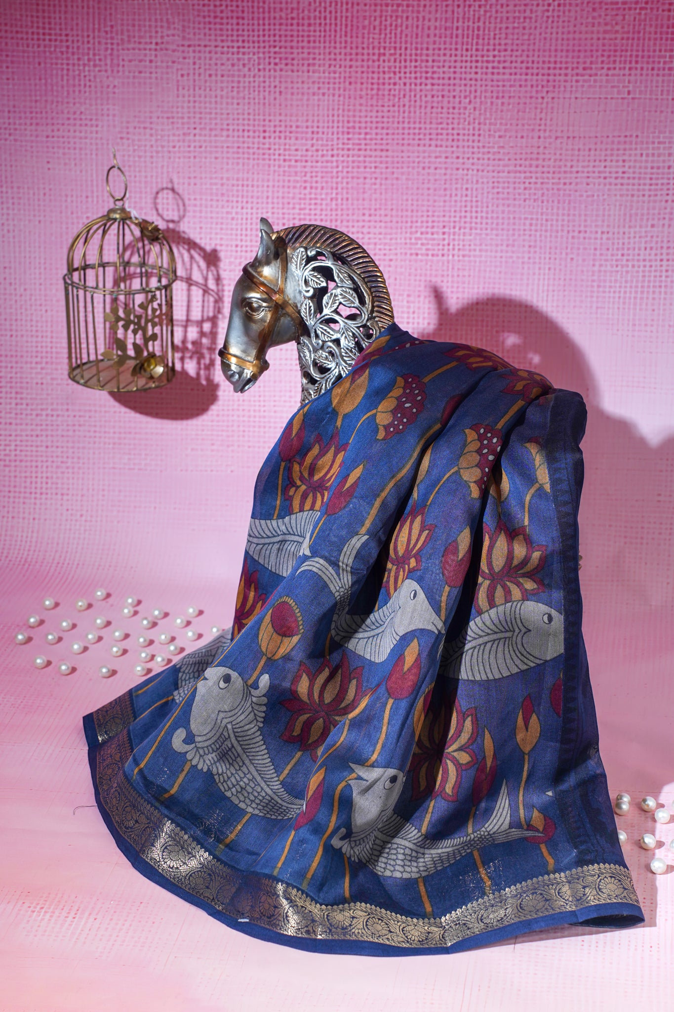 Decorative scarf with horse and Blue saree with Fish and floral patterns draped over a horse head sculpture on a pink background.
